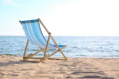 Photo of Empty cozy lounger on sand near sea, space for text. Beach objects