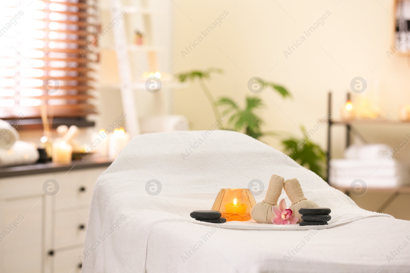 Photo of Composition with herbal bags, candle and stones on massage table in spa salon. Space for text