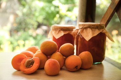 Photo of Delicious ripe apricots with jars of homemade jam on wooden table outdoors