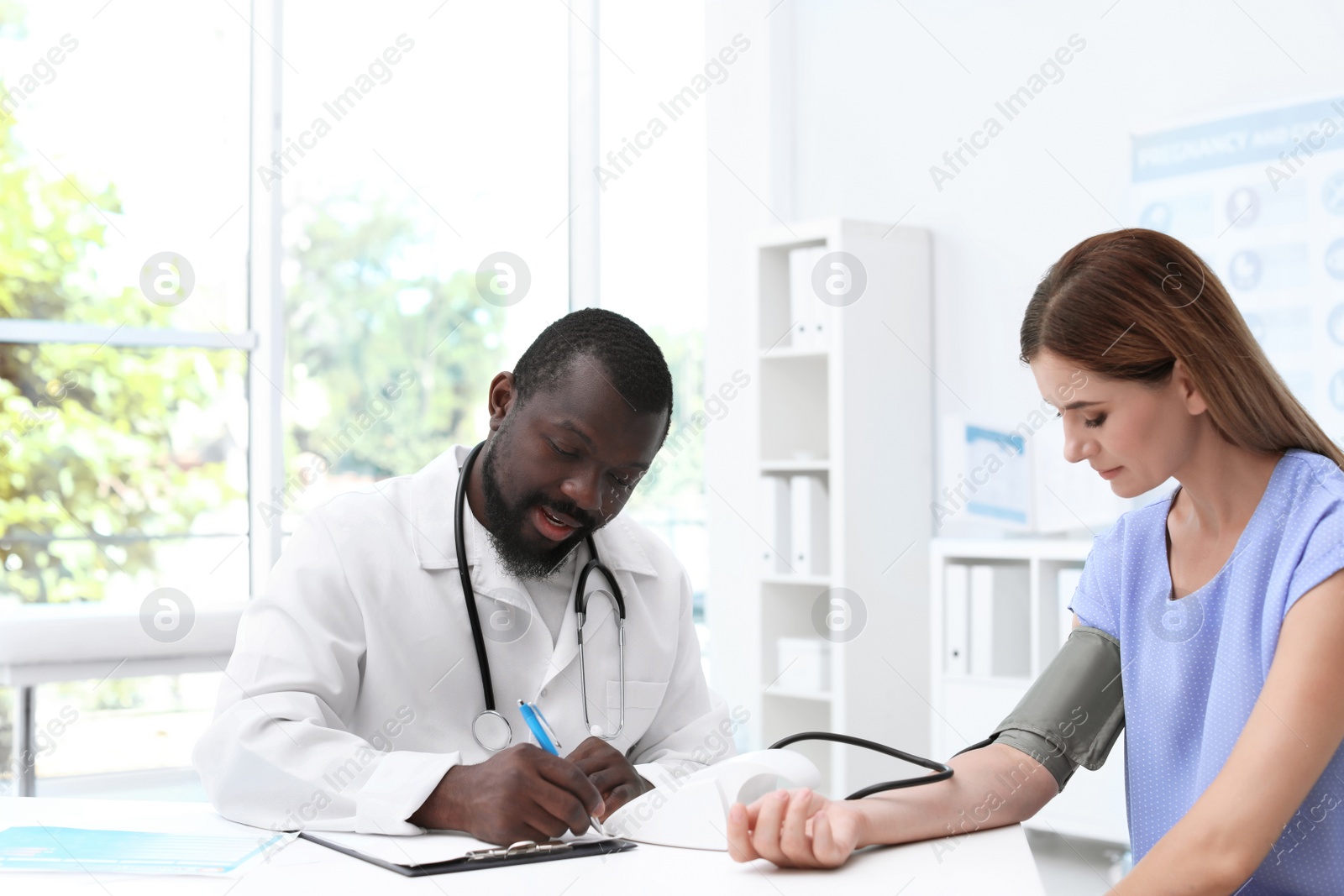 Photo of Young African-American doctor checking patient's blood pressure in hospital