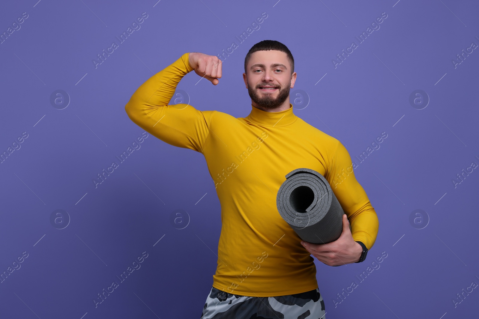 Photo of Handsome sportsman with fitness mat on purple background