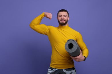 Photo of Handsome sportsman with fitness mat on purple background