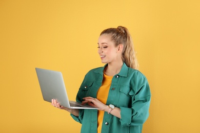 Portrait of beautiful young woman with laptop on yellow background