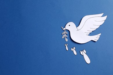 Photo of White paper dove with olive branch and bombs on blue background, flat lay. Space for text