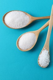 Organic white salt in spoons on light blue background, flat lay