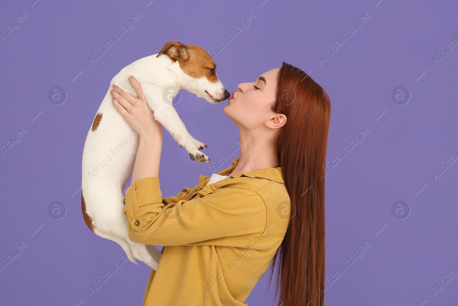 Photo of Woman kissing her cute Jack Russell Terrier dog on violet background