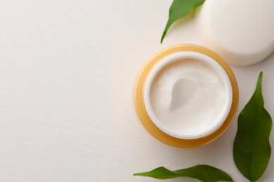 Photo of Jar of face cream and green leaves on white background, flat lay. Space for text