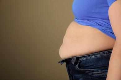 Photo of Overweight woman in tight shirt and jeans on light brown background, closeup. Space for text