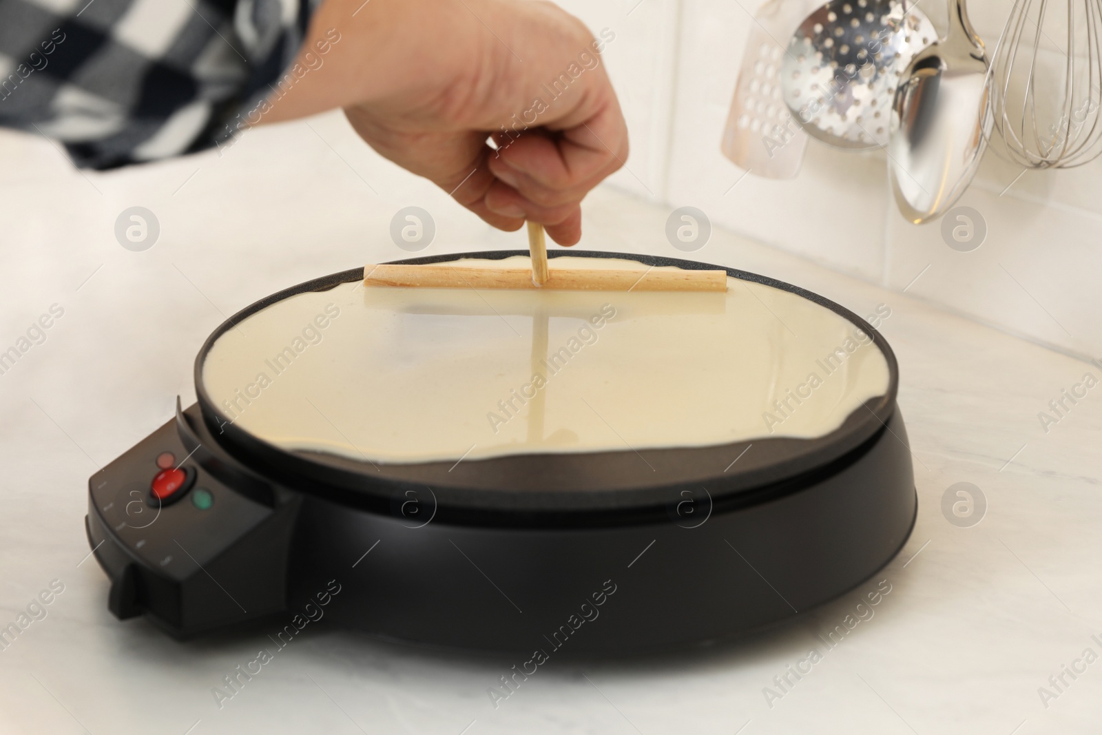 Photo of Man cooking delicious crepe on electric pancake maker in kitchen, closeup