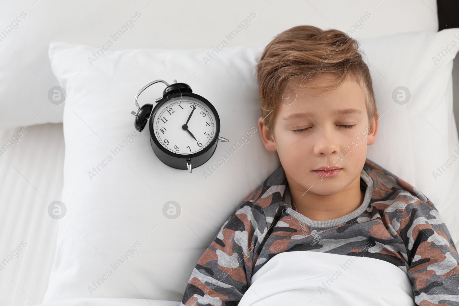 Photo of Cute boy with alarm clock sleeping in bed, above view