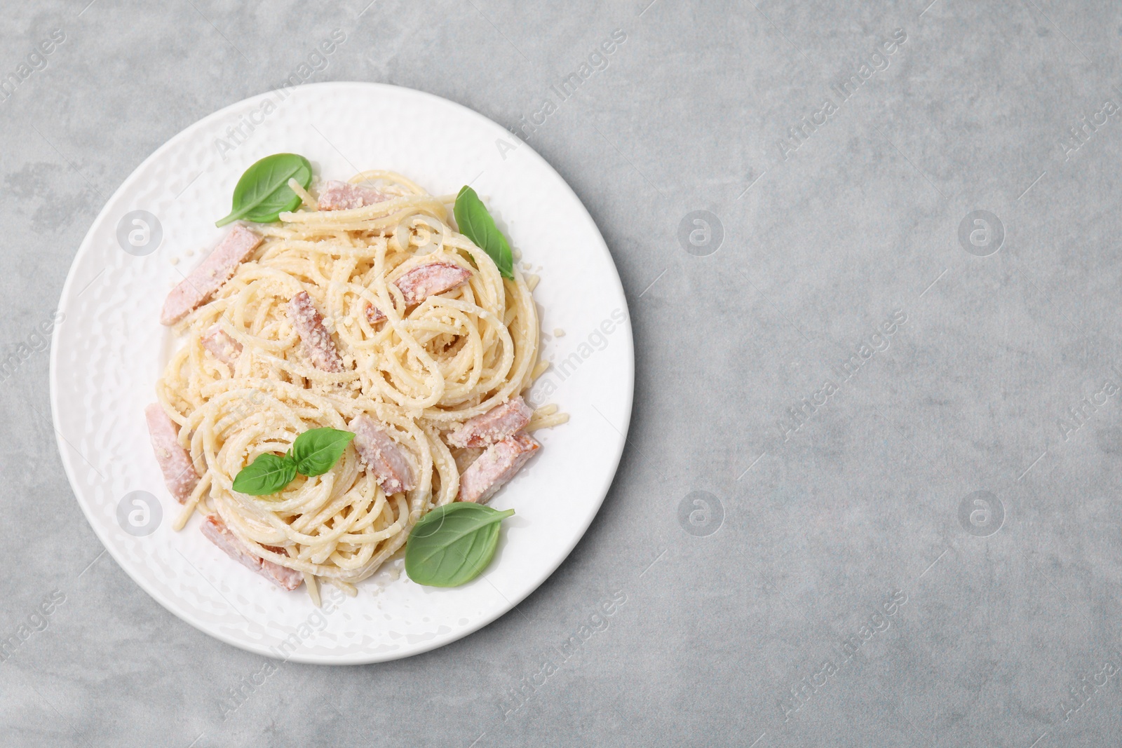 Photo of Plate of tasty pasta Carbonara with basil leaves on grey table, top view. Space for text
