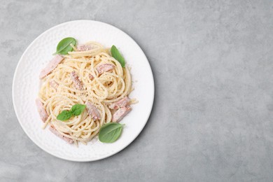 Plate of tasty pasta Carbonara with basil leaves on grey table, top view. Space for text