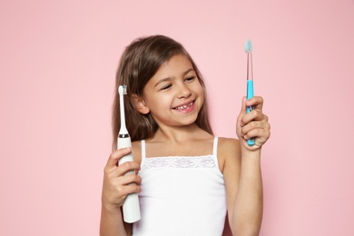 Little girl choosing between manual and electric toothbrushes on color background