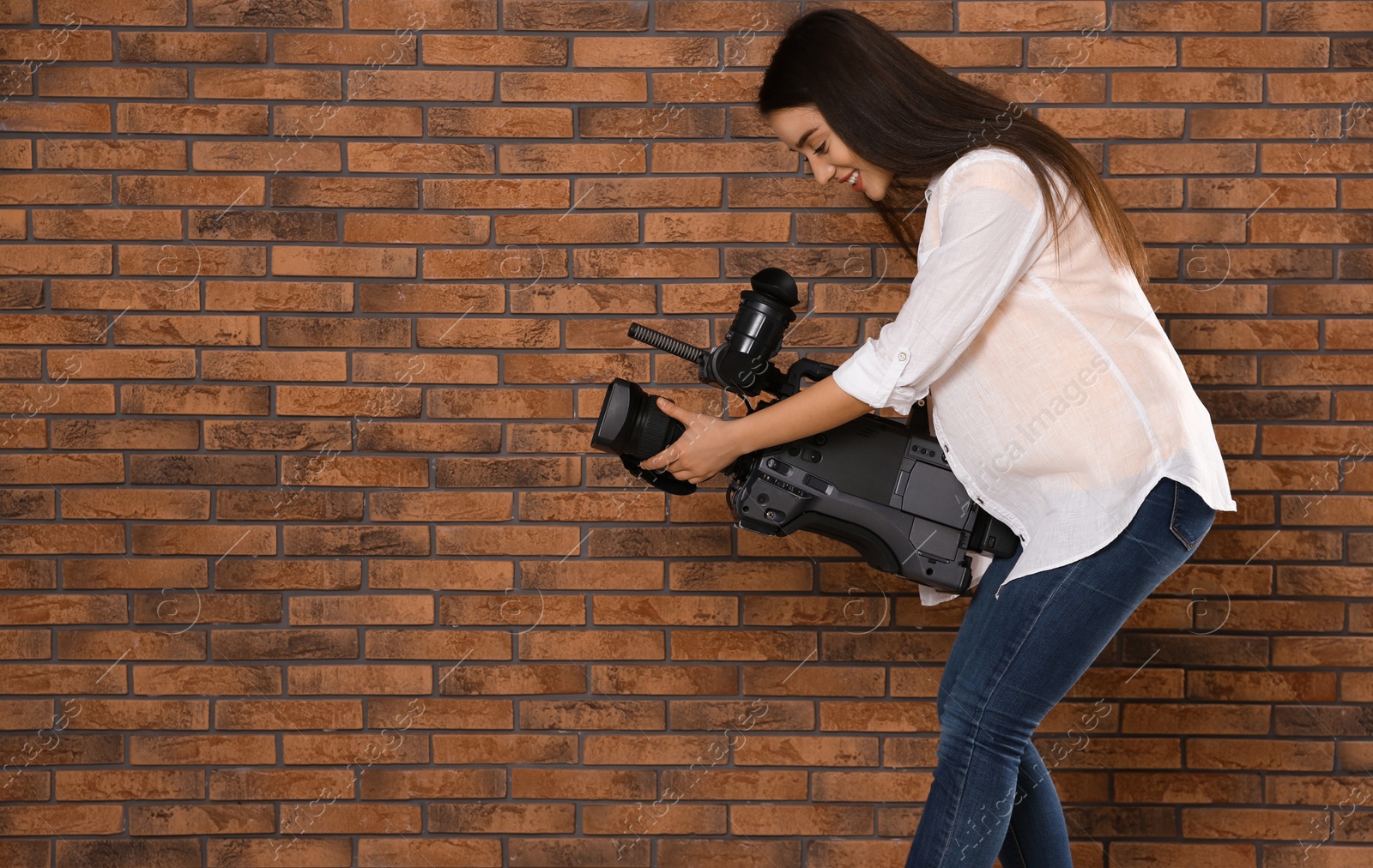 Photo of Operator with professional video camera near brick wall, space for text