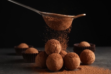 Photo of Tasty chocolate truffles powdered with cocoa from sieve on grey table