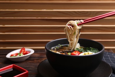 Photo of Eating delicious vegetarian ramen with chopsticks at wooden table, space for text. Noodle soup