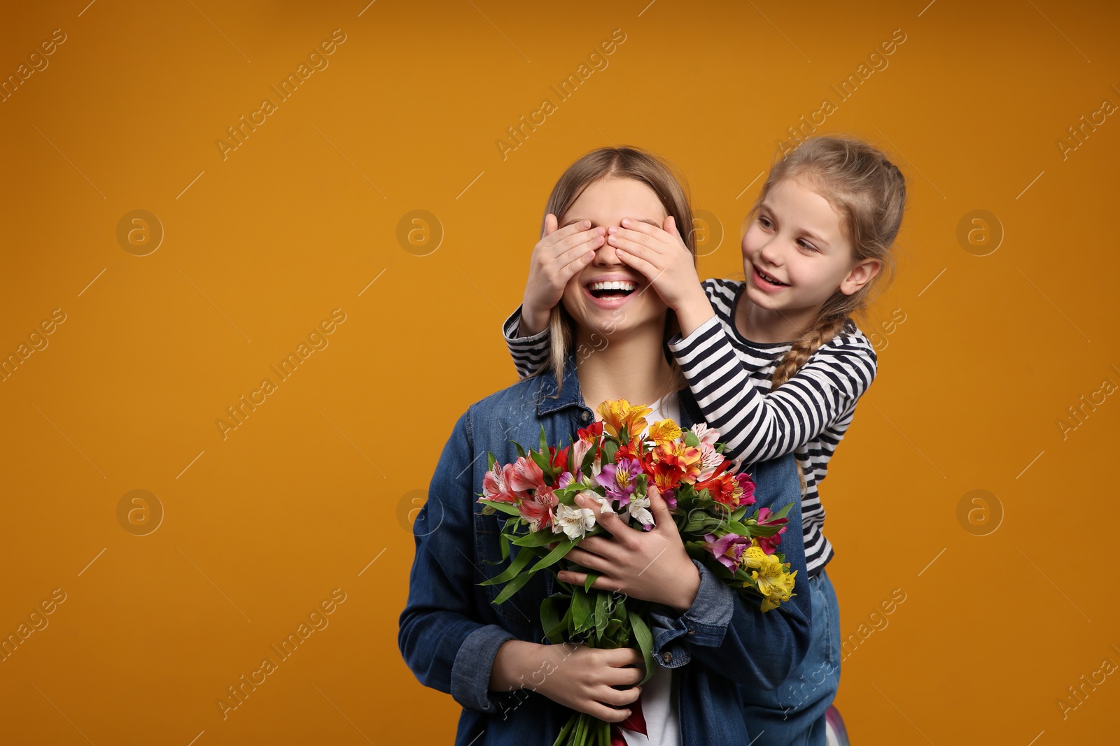 Photo of Little daughter congratulating her mom with flowers on orange background, space for text. Happy Mother's Day