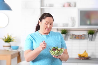 Overweight woman with bowl of salad in kitchen. Healthy diet