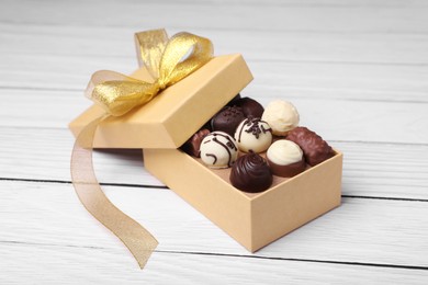 Photo of Box with tasty chocolate candies on white wooden table