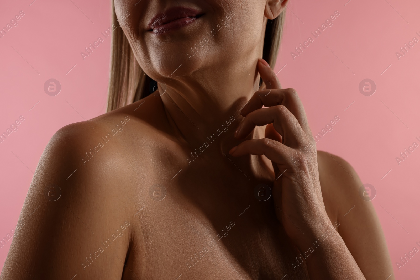 Photo of Mature woman touching her neck on pink background, closeup