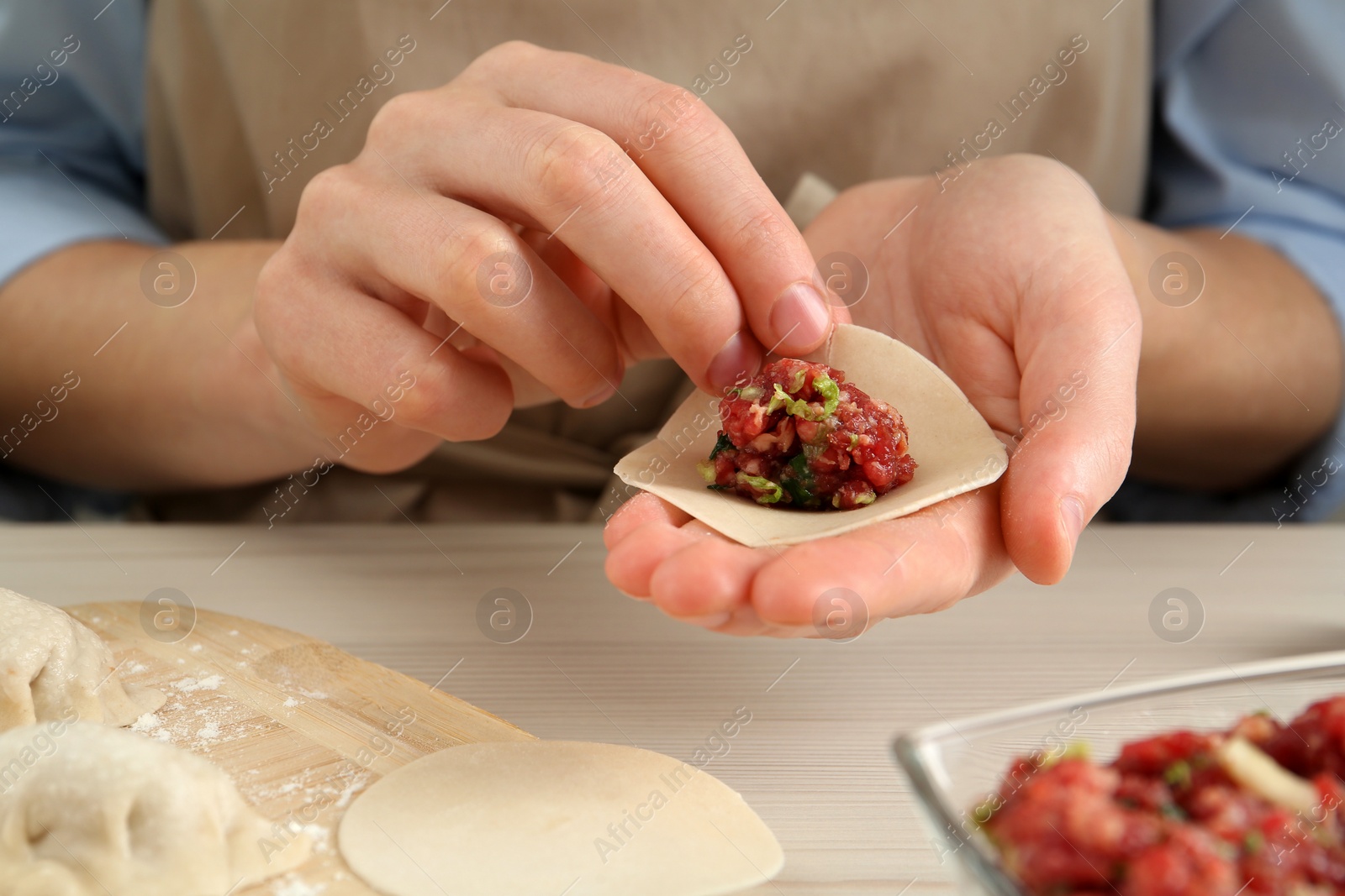 Photo of Woman making gyoza at white wooden table, closeup