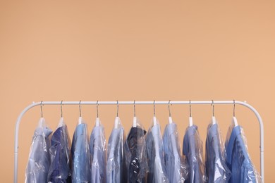 Photo of Dry-cleaning service. Many different clothes in plastic bags hanging on rack against beige background, space for text