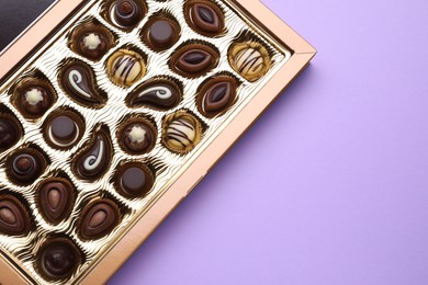 Box of delicious chocolate candies on violet background, top view. Space for text