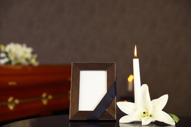 Photo of Black photo frame with burning candle and white lily on table in funeral home