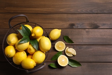 Many fresh ripe lemons with green leaves on wooden table, flat lay. Space for text