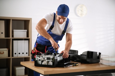 Repairman with screwdriver fixing modern printer in office