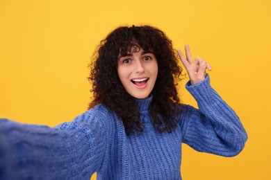 Beautiful young woman taking selfie on orange background