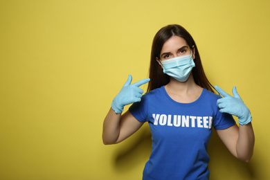 Photo of Female volunteer in mask and gloves on yellow background, space for text. Protective measures during coronavirus quarantine