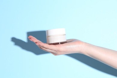 Woman holding jar of cream on light blue background, closeup