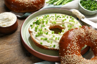 Delicious bagel with cream cheese and green onion on wooden table, closeup