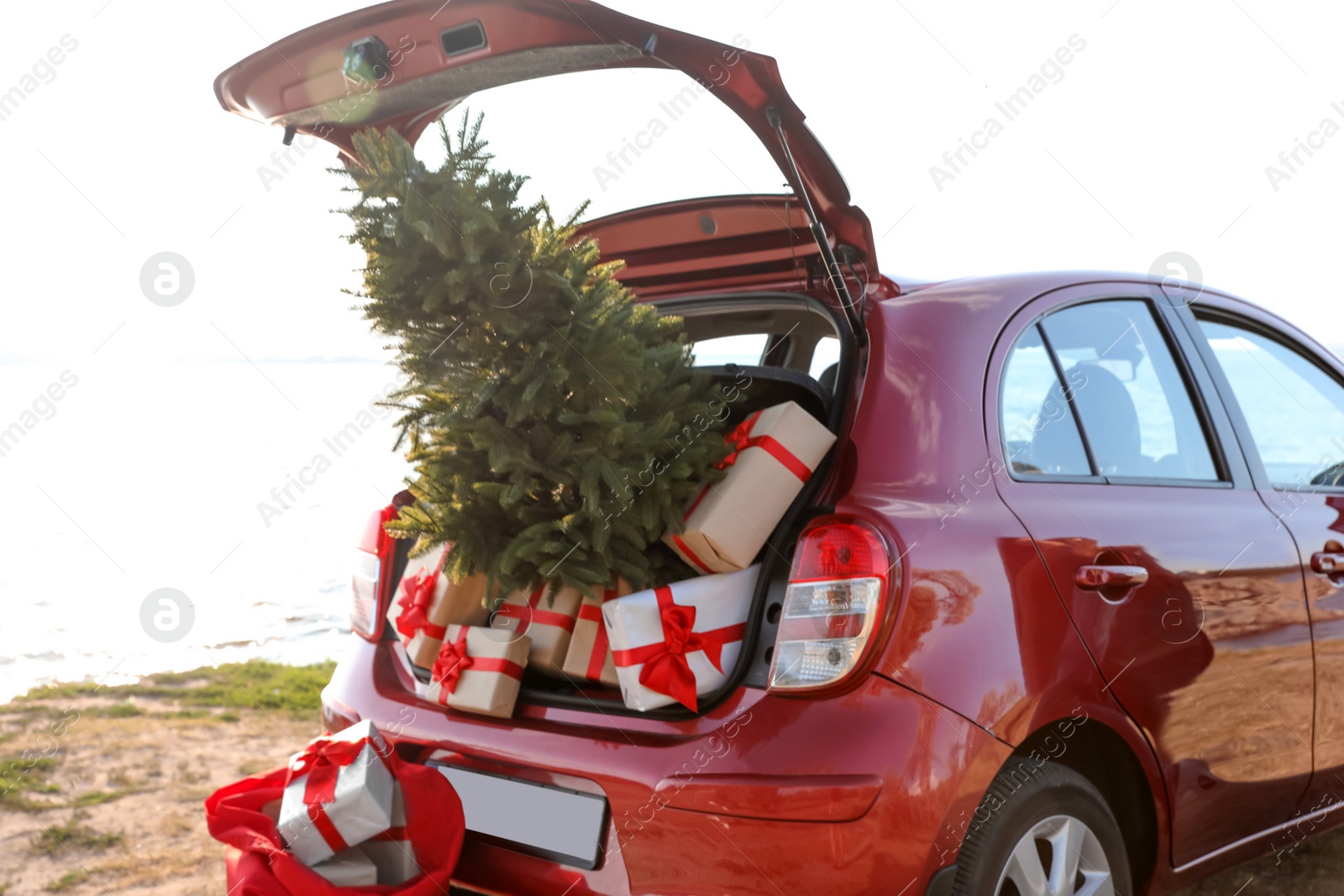 Photo of Red car with gift boxes and Christmas tree on beach. Santa Claus delivery