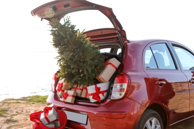 Photo of Red car with gift boxes and Christmas tree on beach. Santa Claus delivery