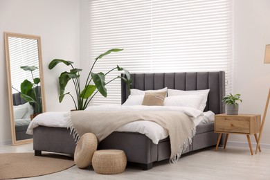 Stylish bedroom interior with large bed, mirror and houseplants