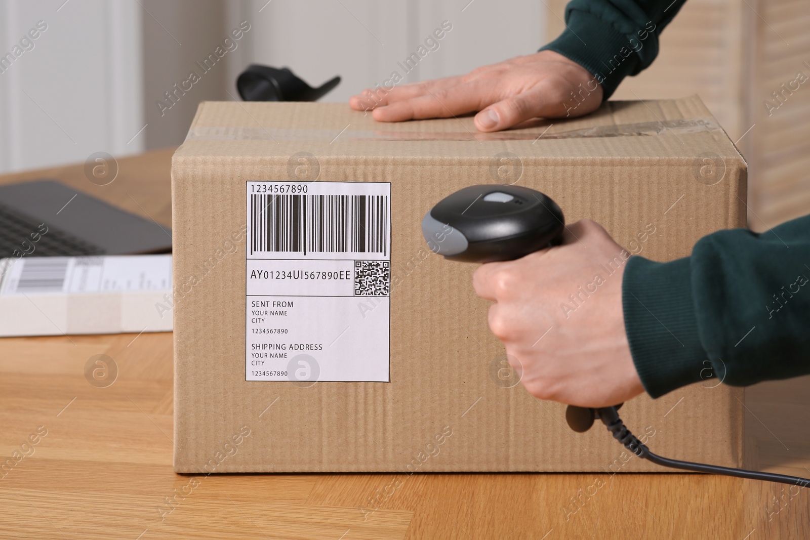 Photo of Seller with scanner reading parcel barcode at table in office, closeup. Online store