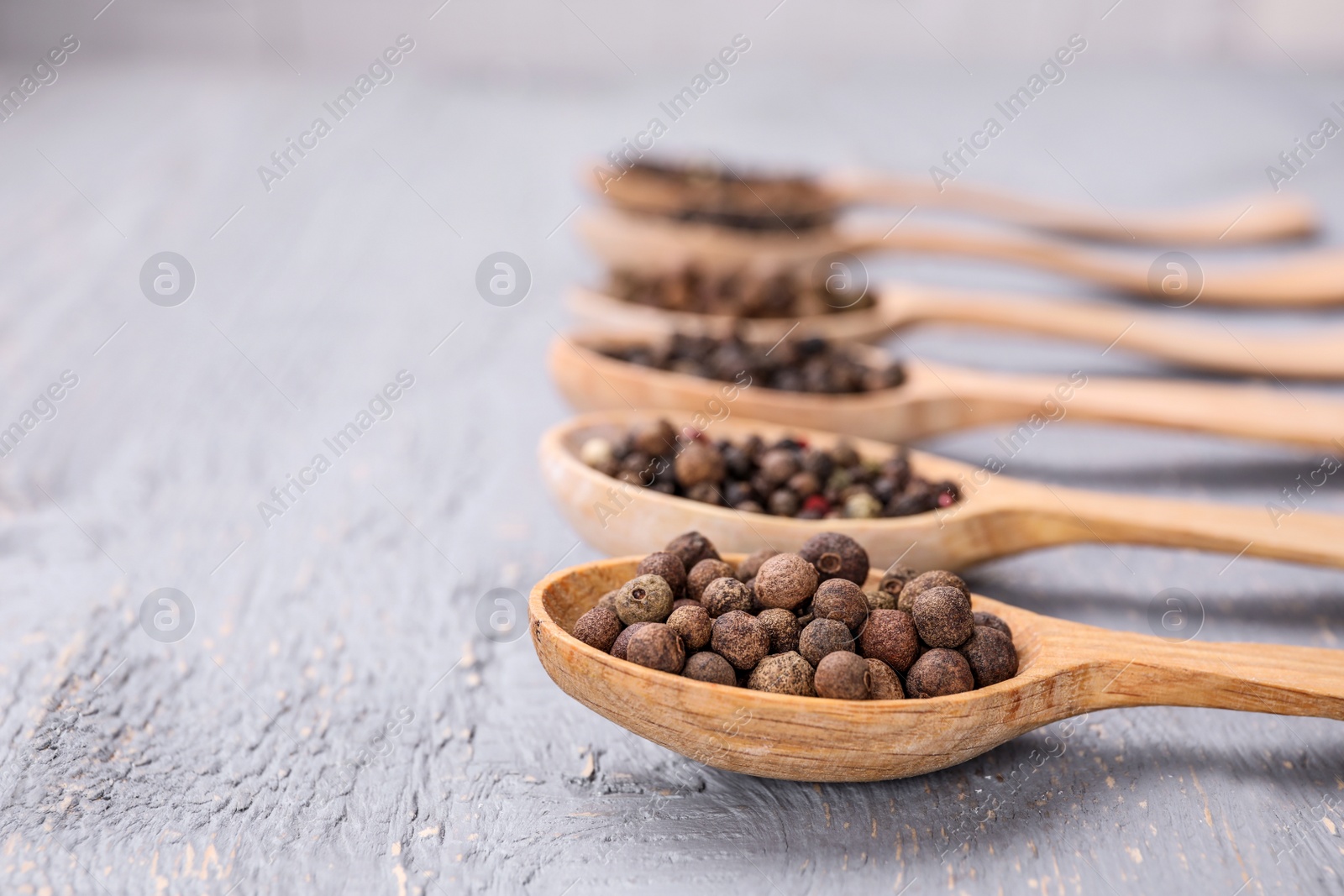 Photo of Spoons with peppercorns on grey wooden table, closeup