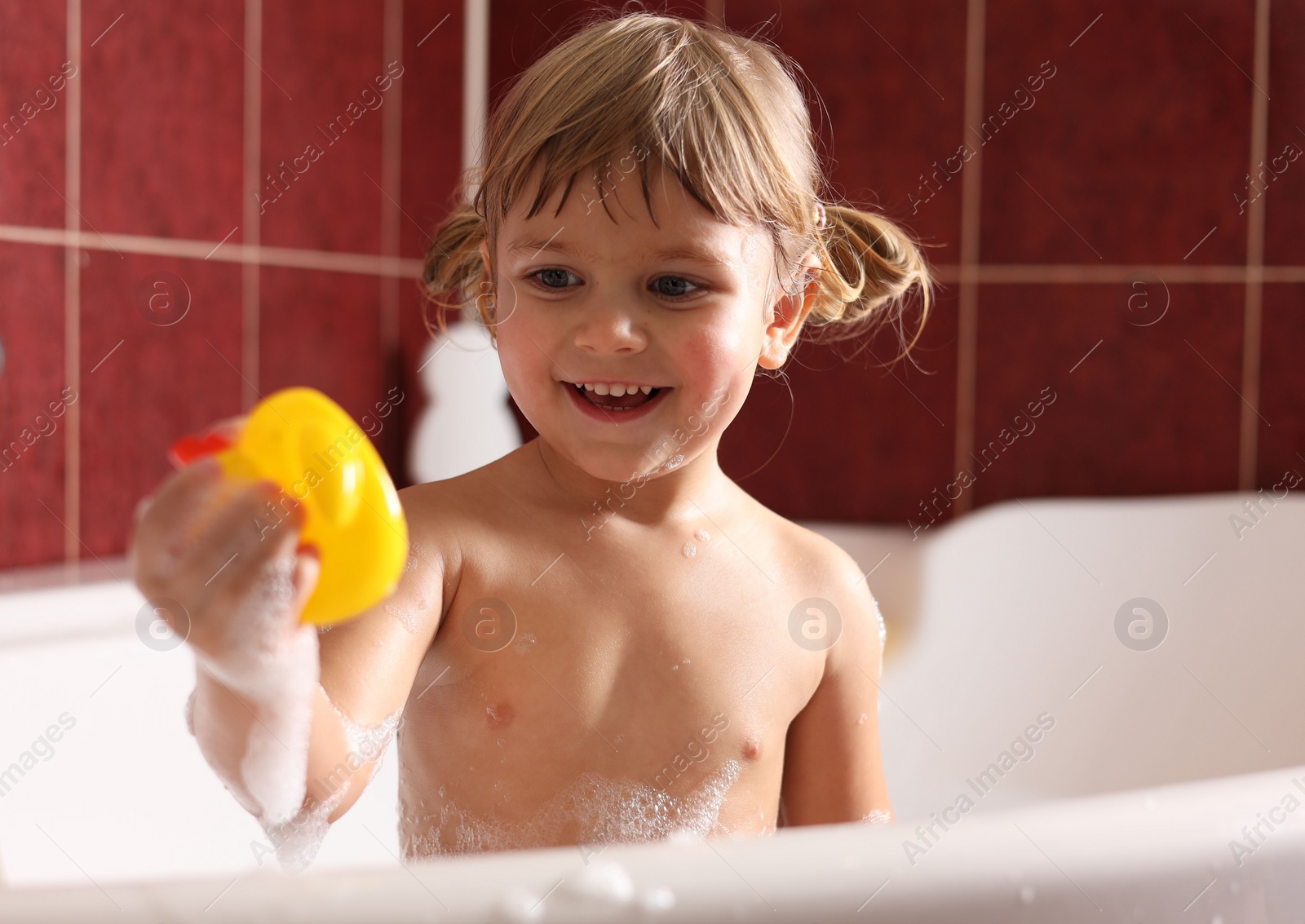 Photo of Smiling girl bathing with toy in tub at home