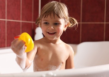 Smiling girl bathing with toy in tub at home