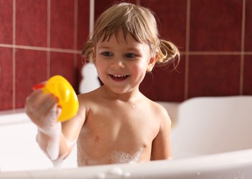 Photo of Smiling girl bathing with toy in tub at home