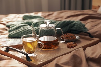 Photo of Wooden tray with freshly brewed tea and cookies on bed in room. Cozy home atmosphere