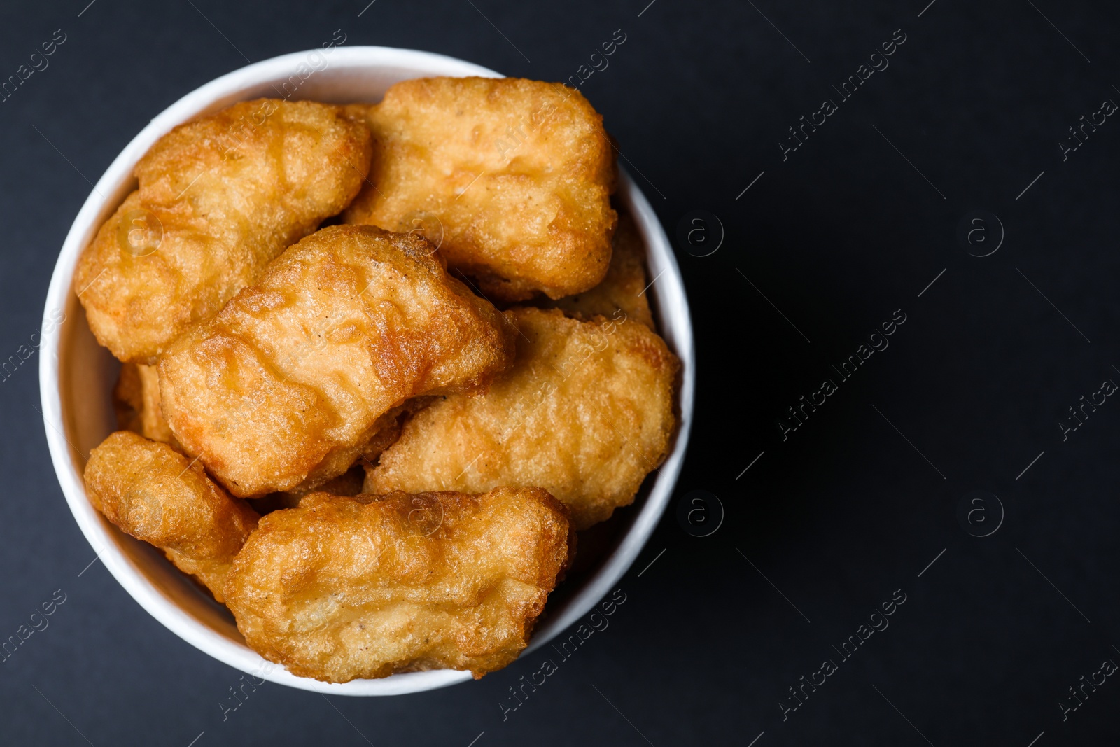 Photo of Bucket with delicious chicken nuggets on black background, top view. Space for text