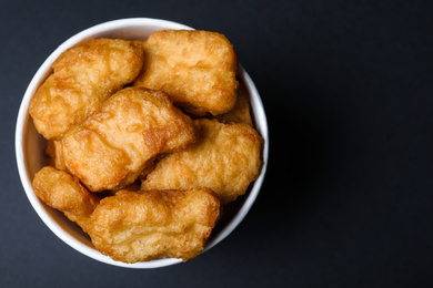 Bucket with delicious chicken nuggets on black background, top view. Space for text