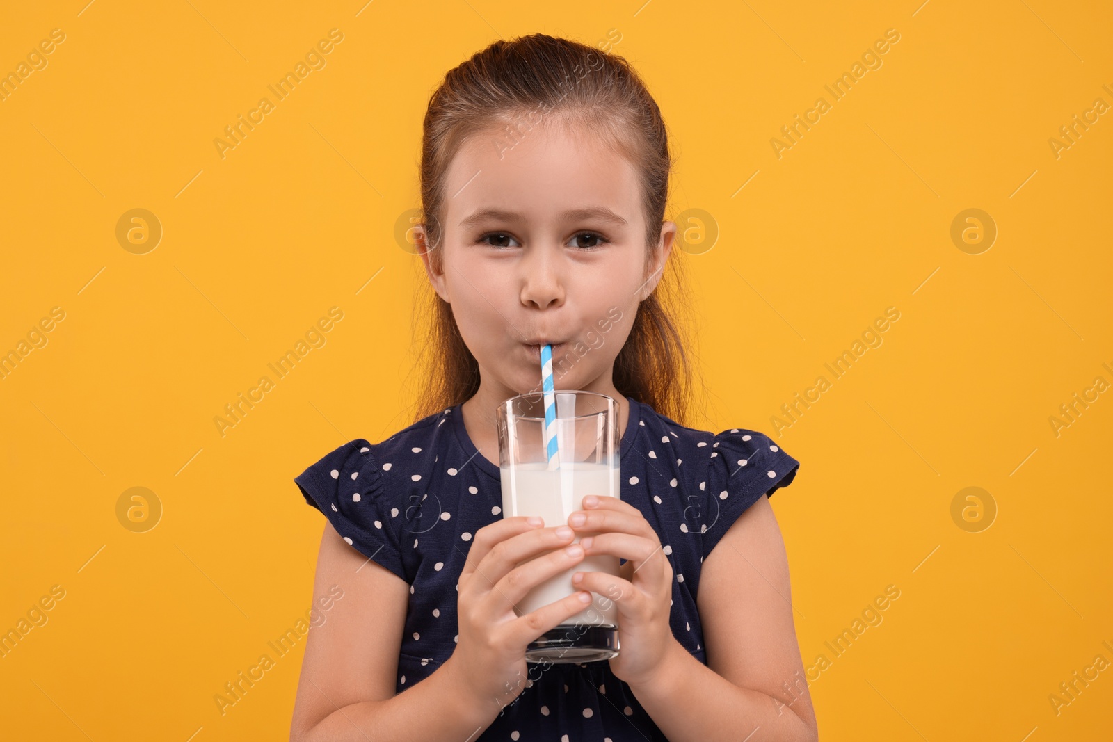 Photo of Cute girl drinking fresh milk from glass on orange background