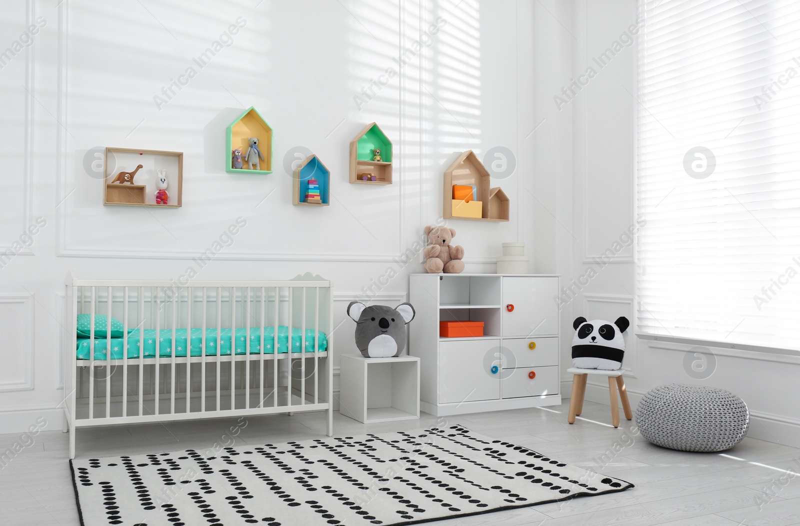 Photo of Comfortable crib near wall with color shelves in baby room. Interior design