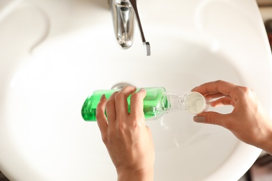 Woman pouring mouthwash from bottle into cap in bathroom, closeup. Teeth care