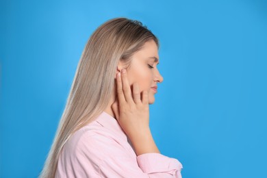 Young woman suffering from ear pain on light blue background. Space for text