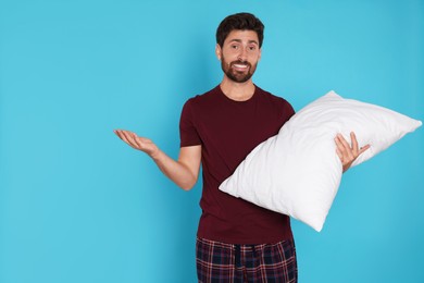 Photo of Handsome man with pillow on light blue background, space for text